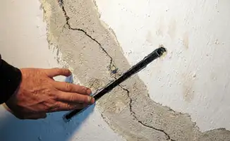 A wall with a large crack is being inspected by a professional in Hialeah, FL